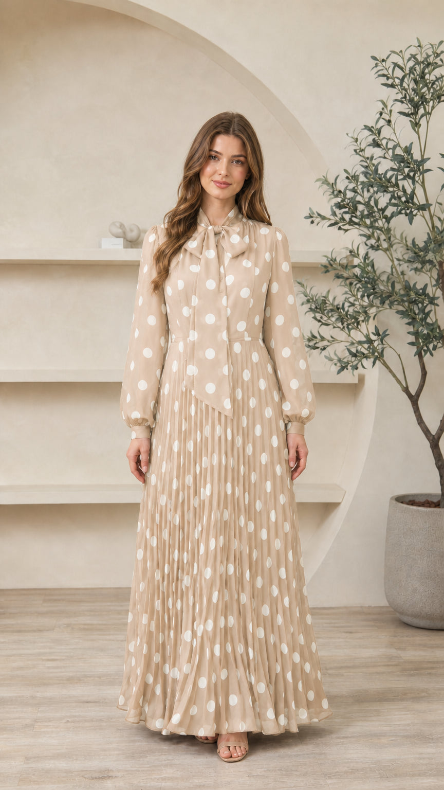Model wearing champagne beige polka dot long sleeve tie-neck pleated maxi dress