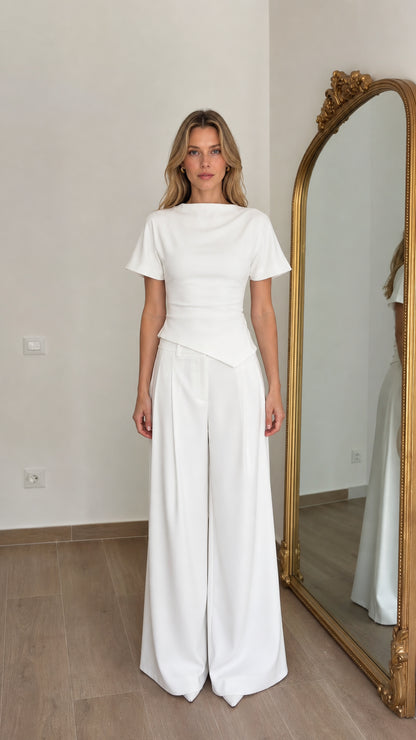 Front view of woman wearing white asymmetric peplum top and wide leg pants set
