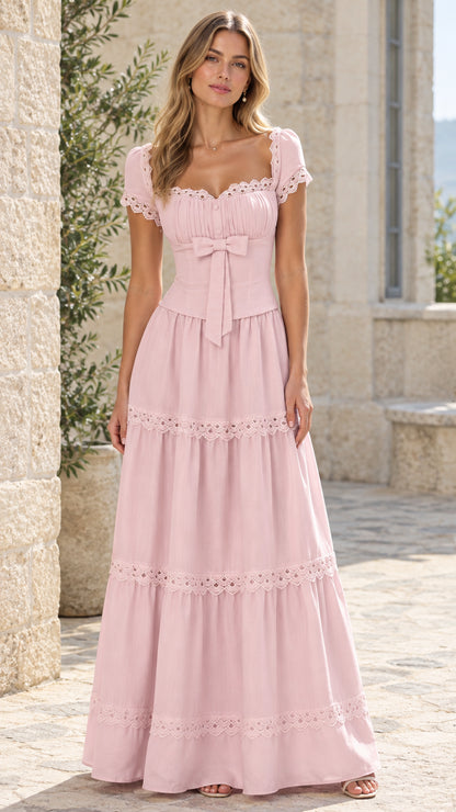 Full-length front view of woman wearing blush pink tiered lace maxi dress in a stone courtyard