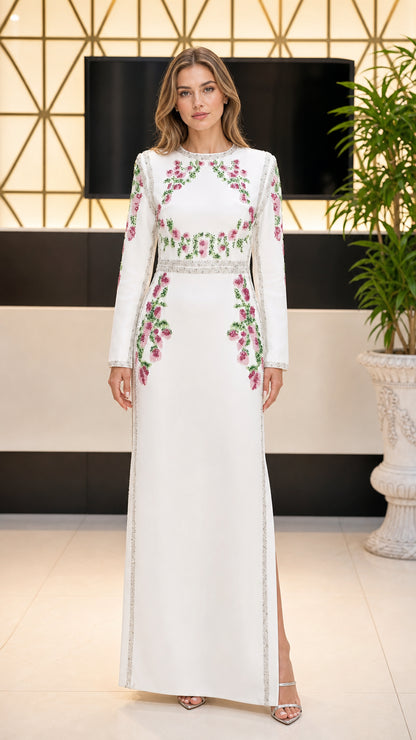 Front view of woman wearing white long sleeve maxi dress with pink floral embroidery and crystal trim