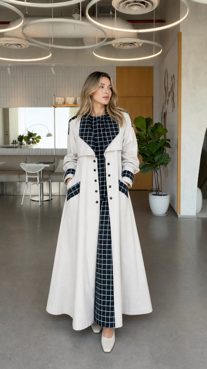 Full front view of model wearing off white maxi trench coat with contrast black and white plaid lapels