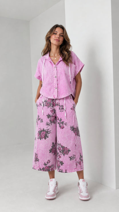 Front full-body view of woman wearing washed pink hooded short-sleeve shirt and floral wide-leg cropped pants set