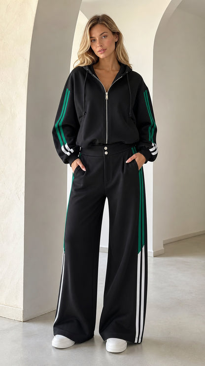 Front full view of woman wearing black 2-piece wide leg tracksuit with green and white side stripes
