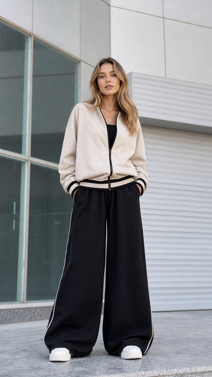 Model wearing beige zip-up bomber jacket and black wide leg track pants front view