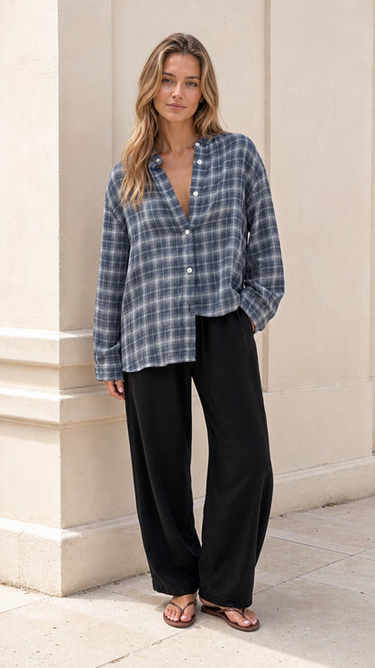 Full front view of model wearing relaxed slate blue plaid band collar button-down shirt with black wide-leg trousers