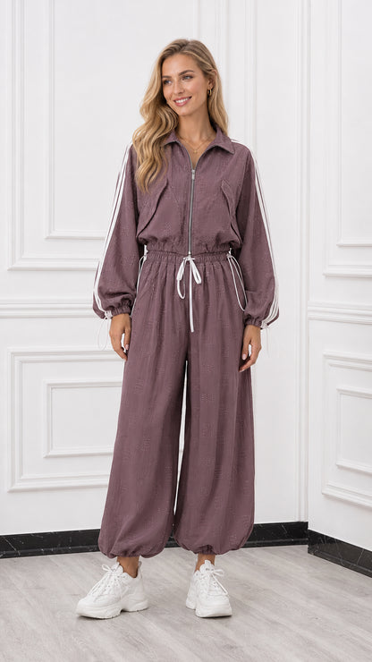 Front view of woman wearing a mauve long sleeve zip-up track jumpsuit with white side stripes