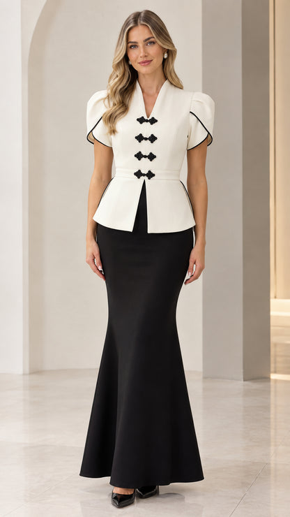 Front full-length view of woman wearing white peplum top with black trim and black mermaid maxi skirt