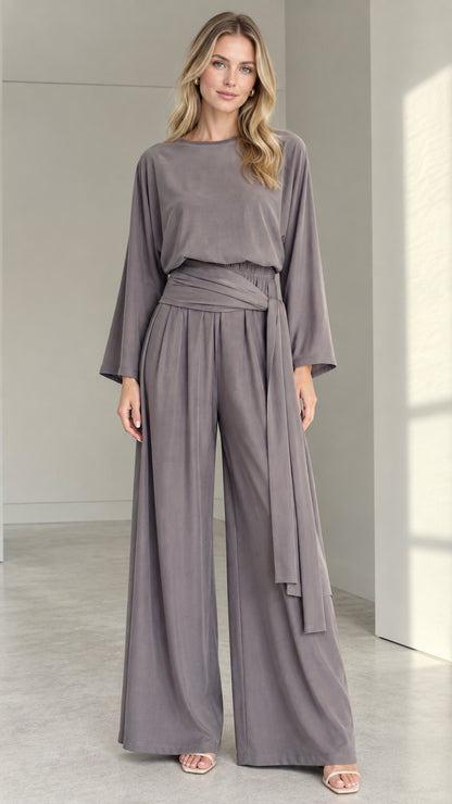 Front full view of woman wearing a slate grey long-sleeve wide-leg jumpsuit with tie waist