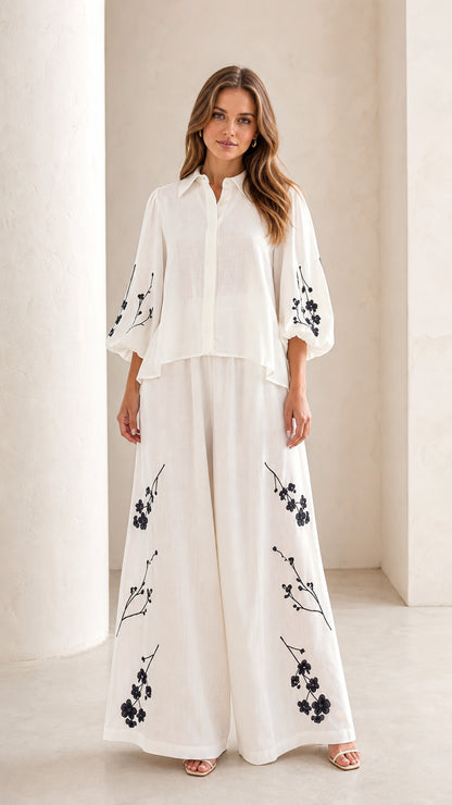 Front full view of woman wearing white floral embroidered blouse and wide-leg pants set