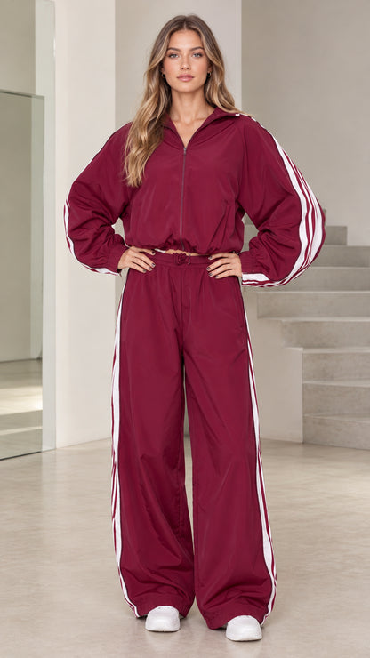 Front view of model wearing burgundy hooded windbreaker tracksuit set with white side stripes