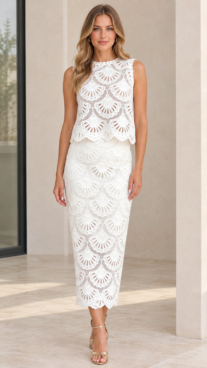 Front view of model wearing white sleeveless scalloped eyelet lace midi dress with strappy gold heels