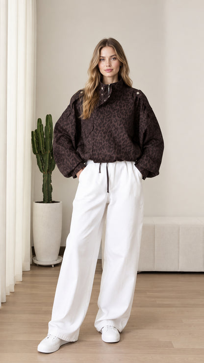 Front view of model wearing chocolate brown leopard print half-zip pullover jacket with white wide-leg pants