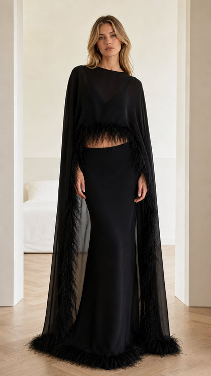 Front view of black two-piece evening gown with feather-trimmed cape top and maxi skirt
