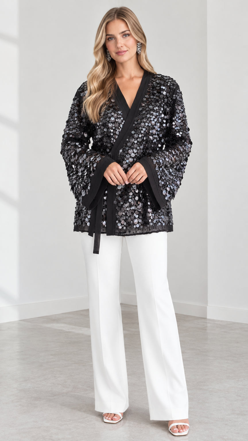 Front view of model wearing Black sequin kimono wrap jacket with waist belt and white pants