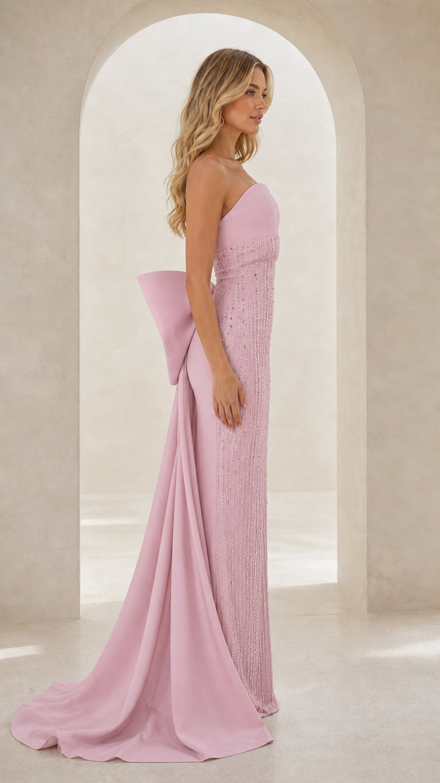 Side profile of model wearing blush pink strapless gown showing the statement back bow and sweep train