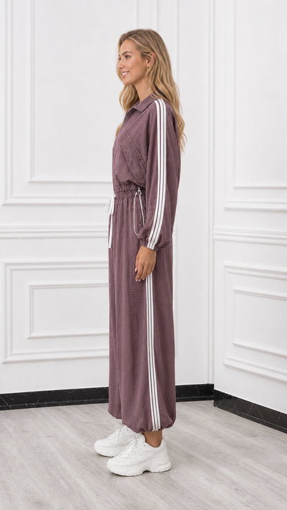 Side profile of woman wearing a mauve sporty jumpsuit with side stripe detail