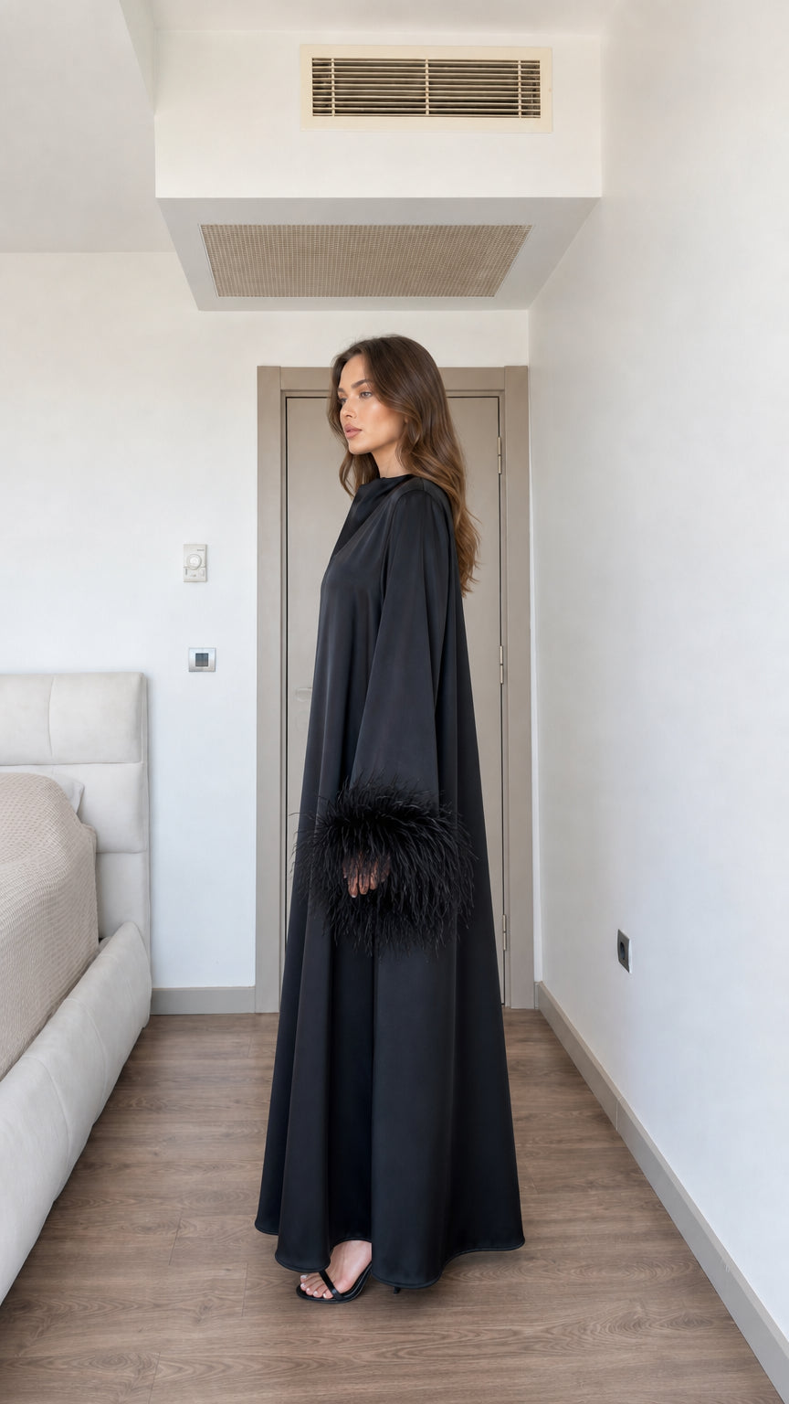 Side profile view of model wearing black satin maxi dress with feather sleeves