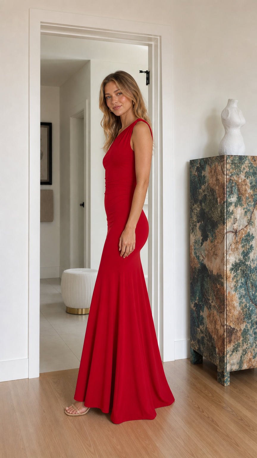 Side profile of model in a fitted red one-shoulder floor-length gown