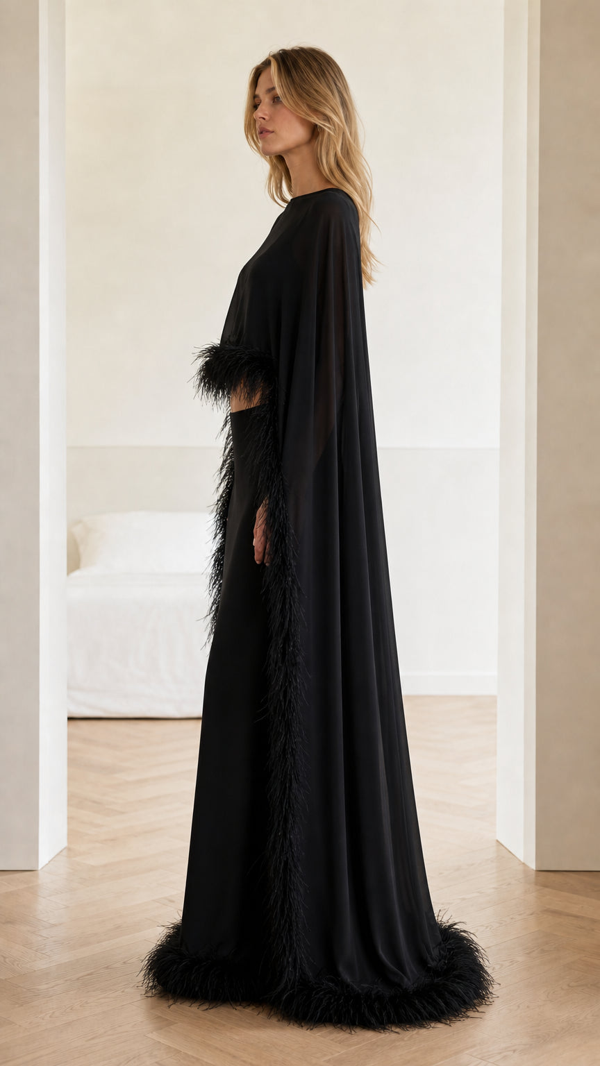 Side profile view of woman wearing black formal cape gown with feather detail