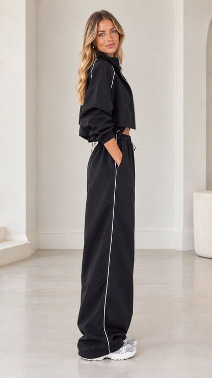 Side profile view of black cropped track jacket and matching side-piped wide leg pants