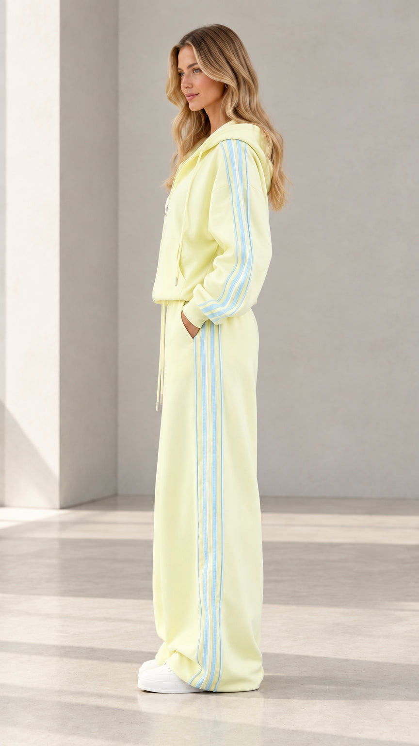 Side profile view of butter yellow two-piece tracksuit showcasing contrast sleeve and pant stripes