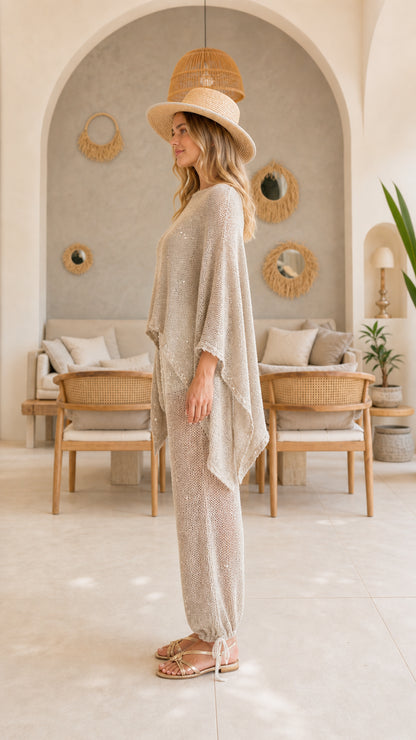Side view of woman wearing beige sequin knit poncho and tie-cuff knit trousers