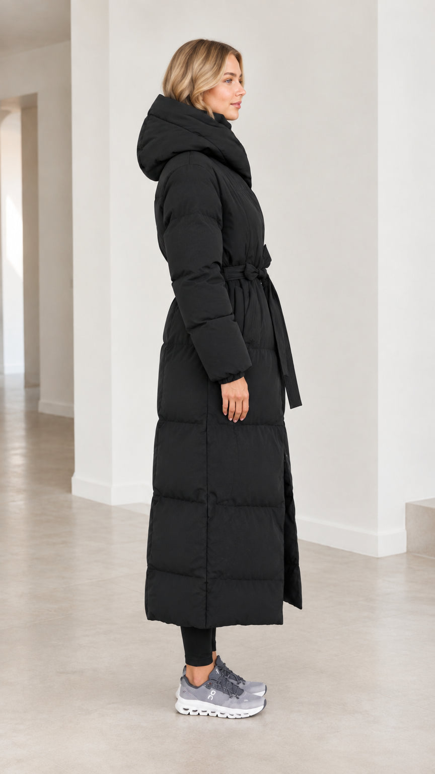 Side profile view of model in black long quilted winter parka coat