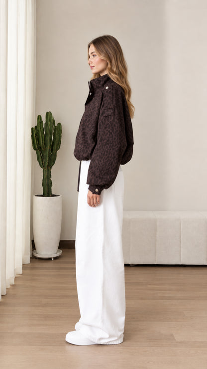 Side profile view of chocolate brown leopard print windbreaker jacket styled with white trousers