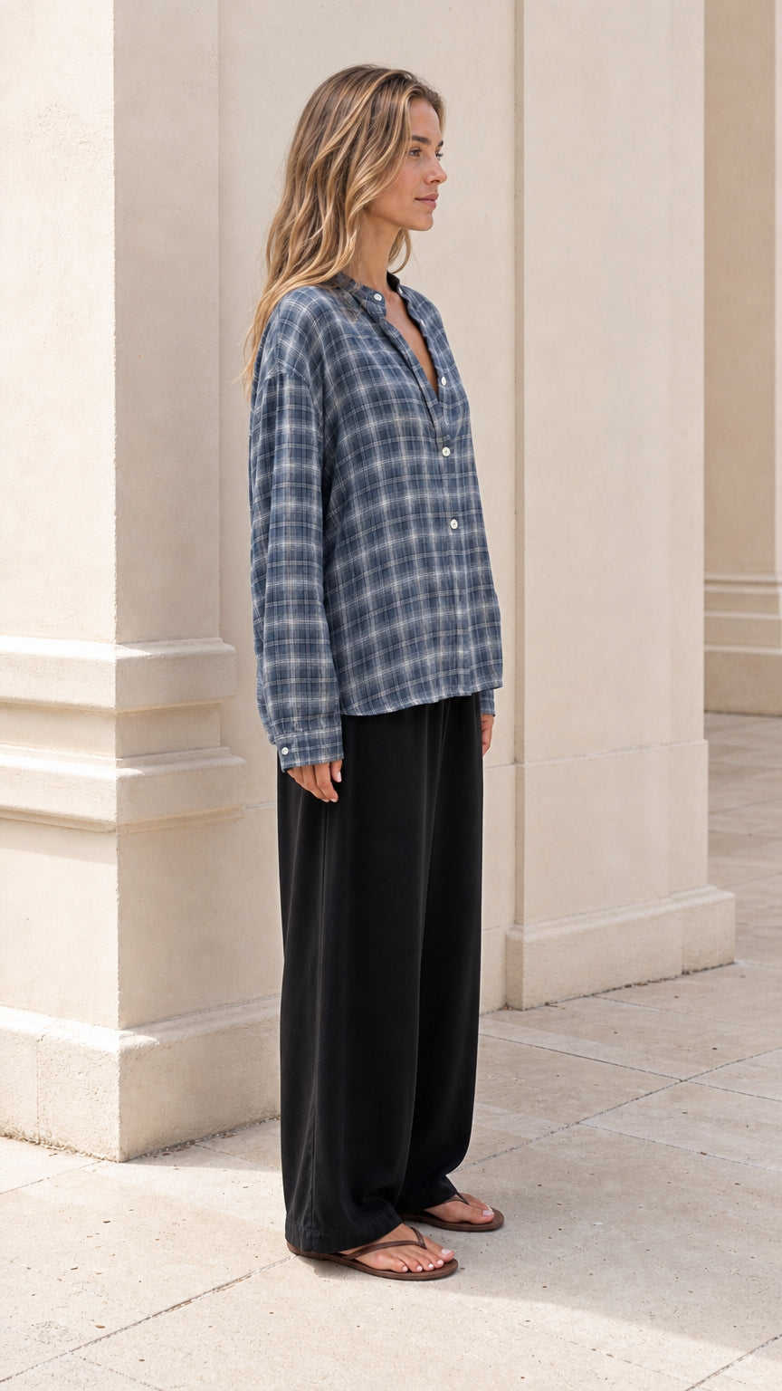 Side angle of model wearing slate blue plaid button-down shirt paired with flowy black trousers