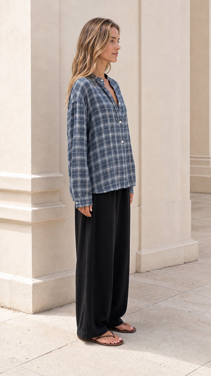 Side angle of model wearing slate blue plaid button-down shirt paired with flowy black trousers