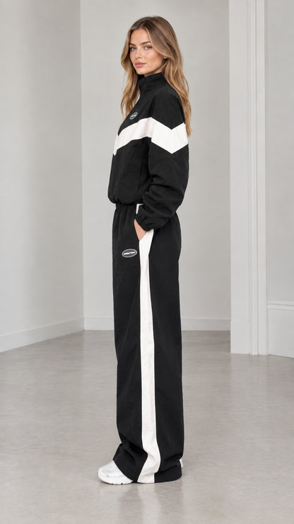 Side profile of woman in black zip-up jacket and wide leg pants with white side stripe