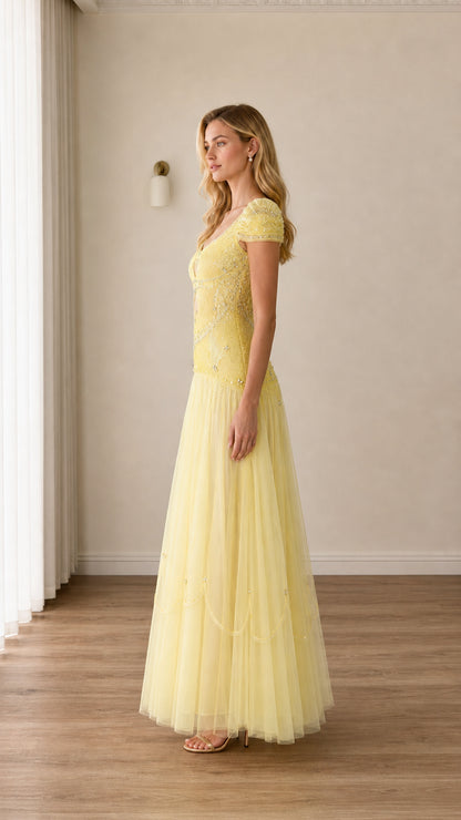 Side profile view of woman modeling pastel yellow beaded floor-length formal dress