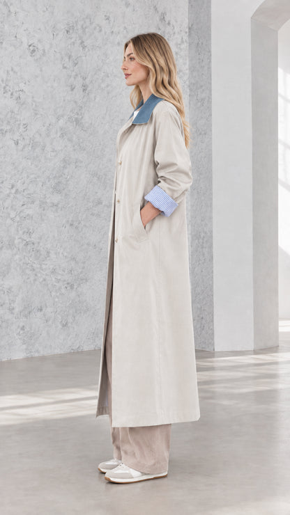 Side profile of woman in full-length light grey duster coat with blue contrast collar