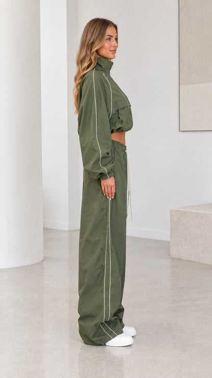 Side profile view of model in olive green tracksuit set showing piping detail