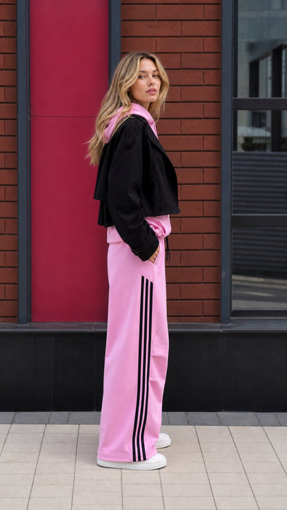 Side profile of pink tracksuit set with black three-stripe detail along pants