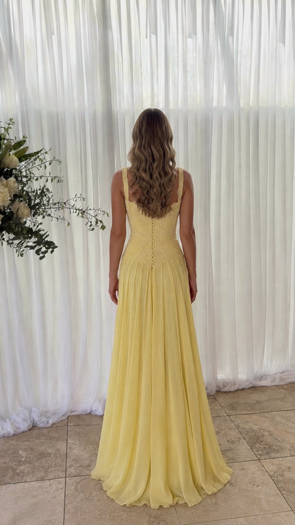 Back view of model wearing yellow chiffon gown showing button-down back detail