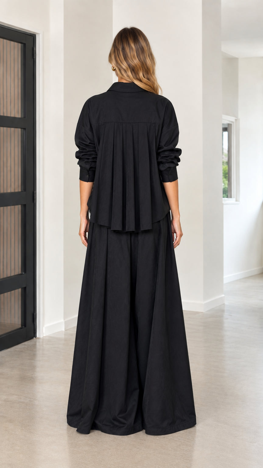 Back view showing dramatic pleated back detail on the black collared shirt and wide pants