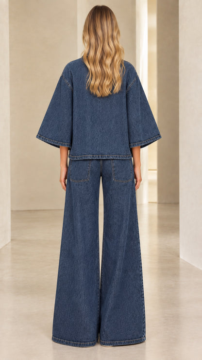 Back view of model wearing Denim Blue flared sleeve denim jacket and wide-leg trousers