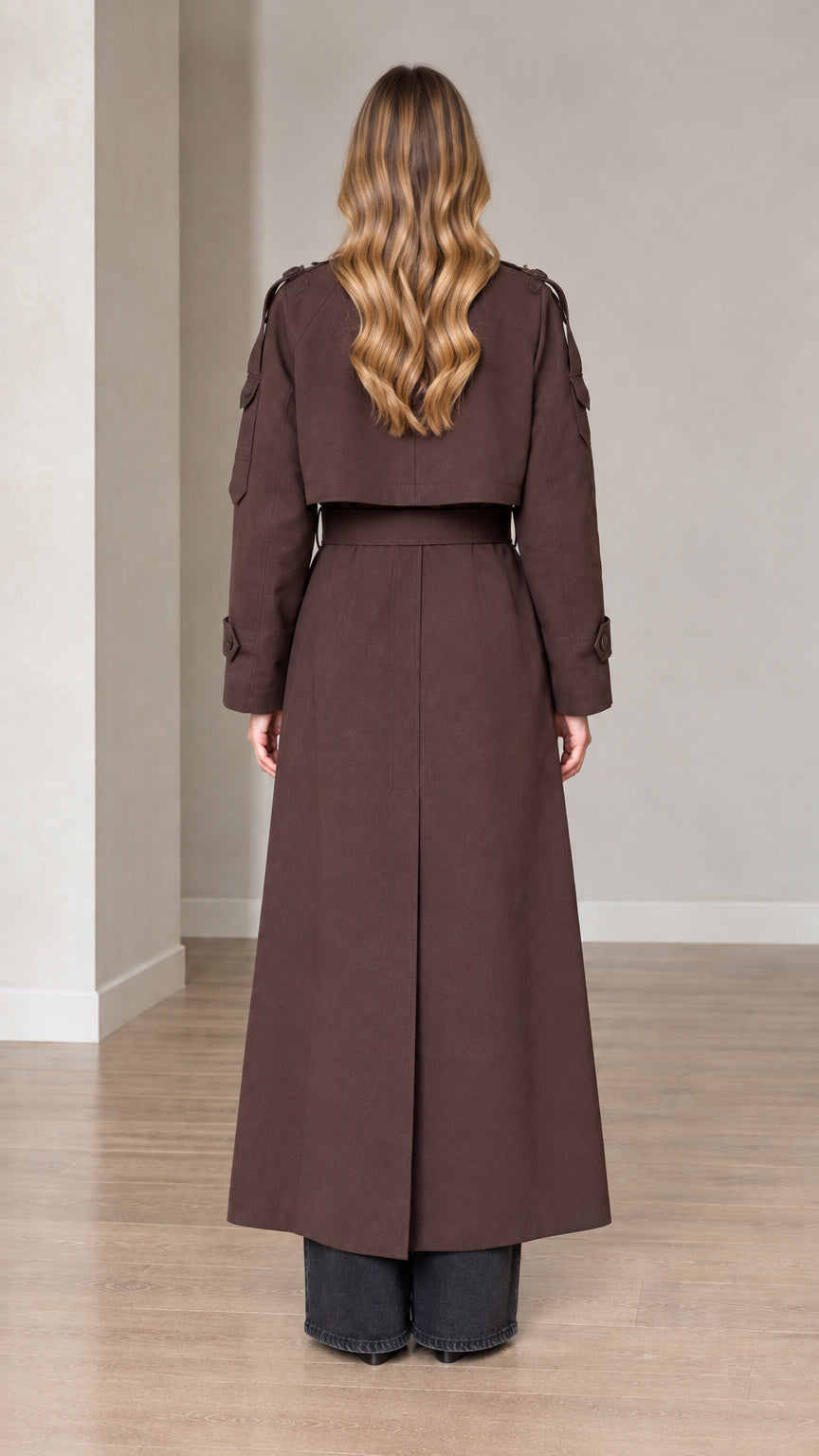 Back view of woman wearing belted brown long trench coat with storm flap