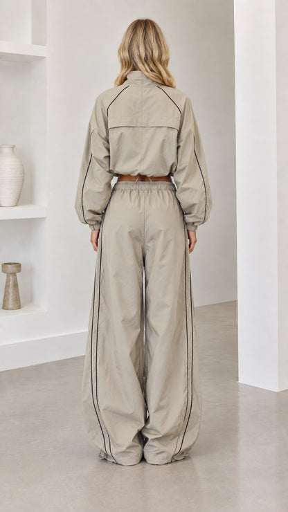 Back view of model wearing taupe cropped jacket and wide-leg parachute pants
