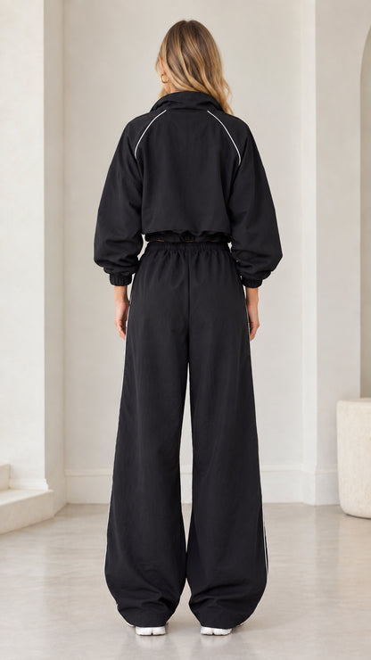 Back view of model in black cropped zip tracksuit set showing contrast piping detail