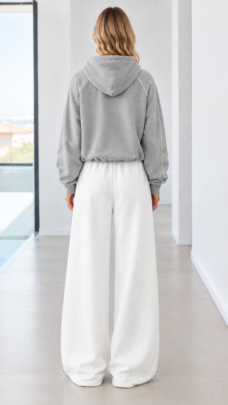 Back view of model wearing grey zip-up hoodie and white wide-leg sweatpants