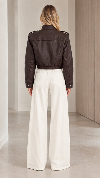 Back view of woman wearing the dark brown cropped faux leather jacket showing back yoke and elastic hem