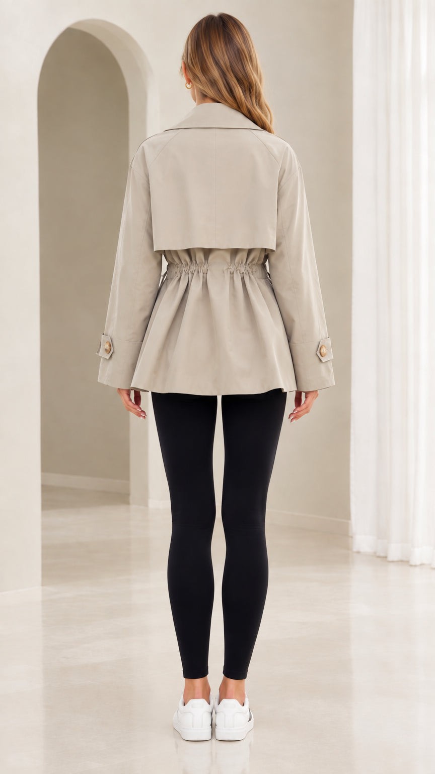 Back view of model wearing khaki short trench jacket showing back storm flap and cinched waist