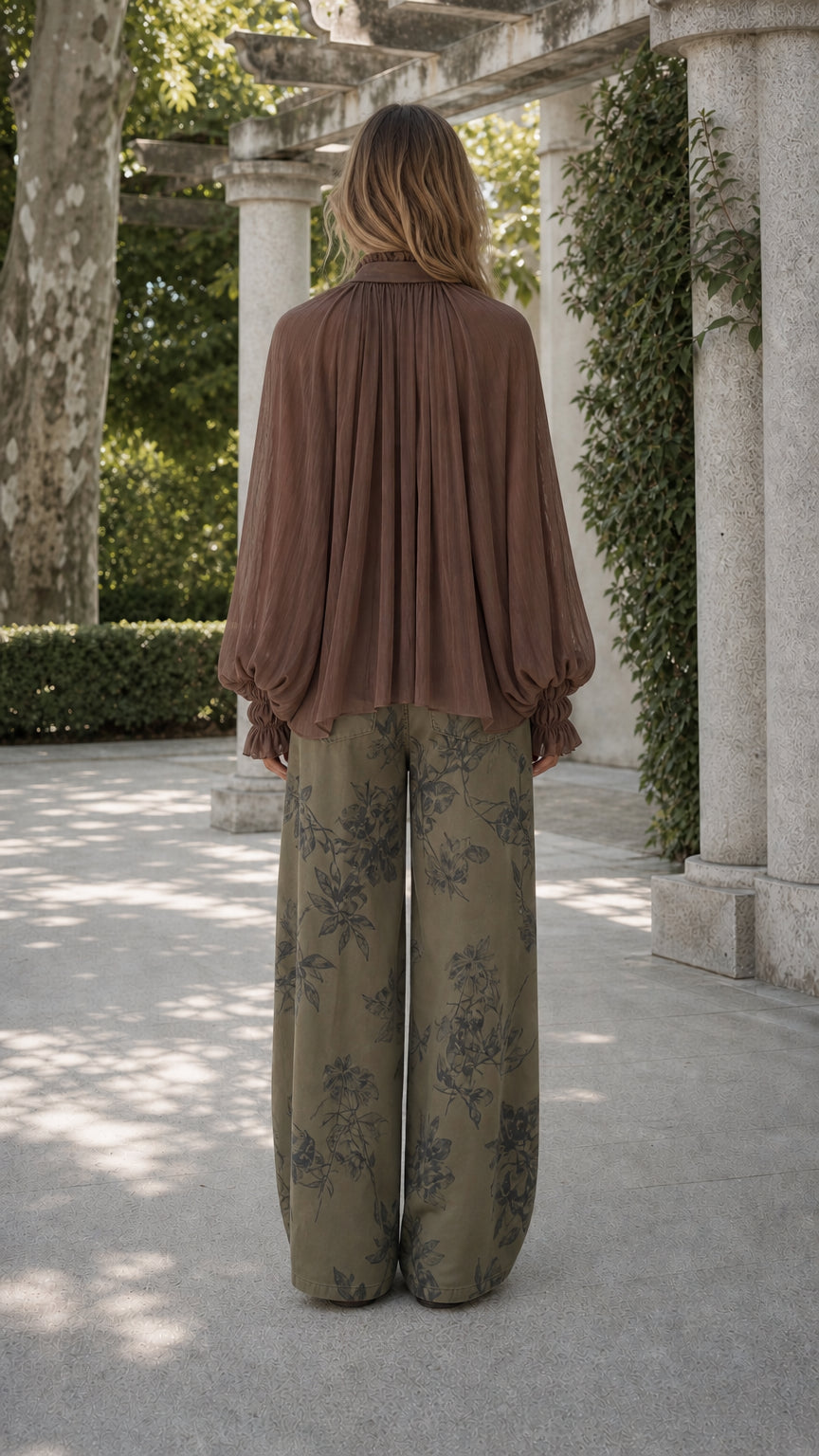 Model back view showing flowing drape of brown ruffled blouse and printed wide-leg pants