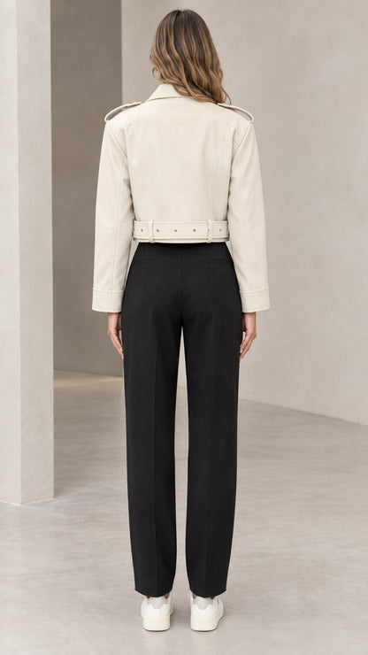 Back view of woman wearing cream cropped faux leather jacket showing waistband and shoulder seams