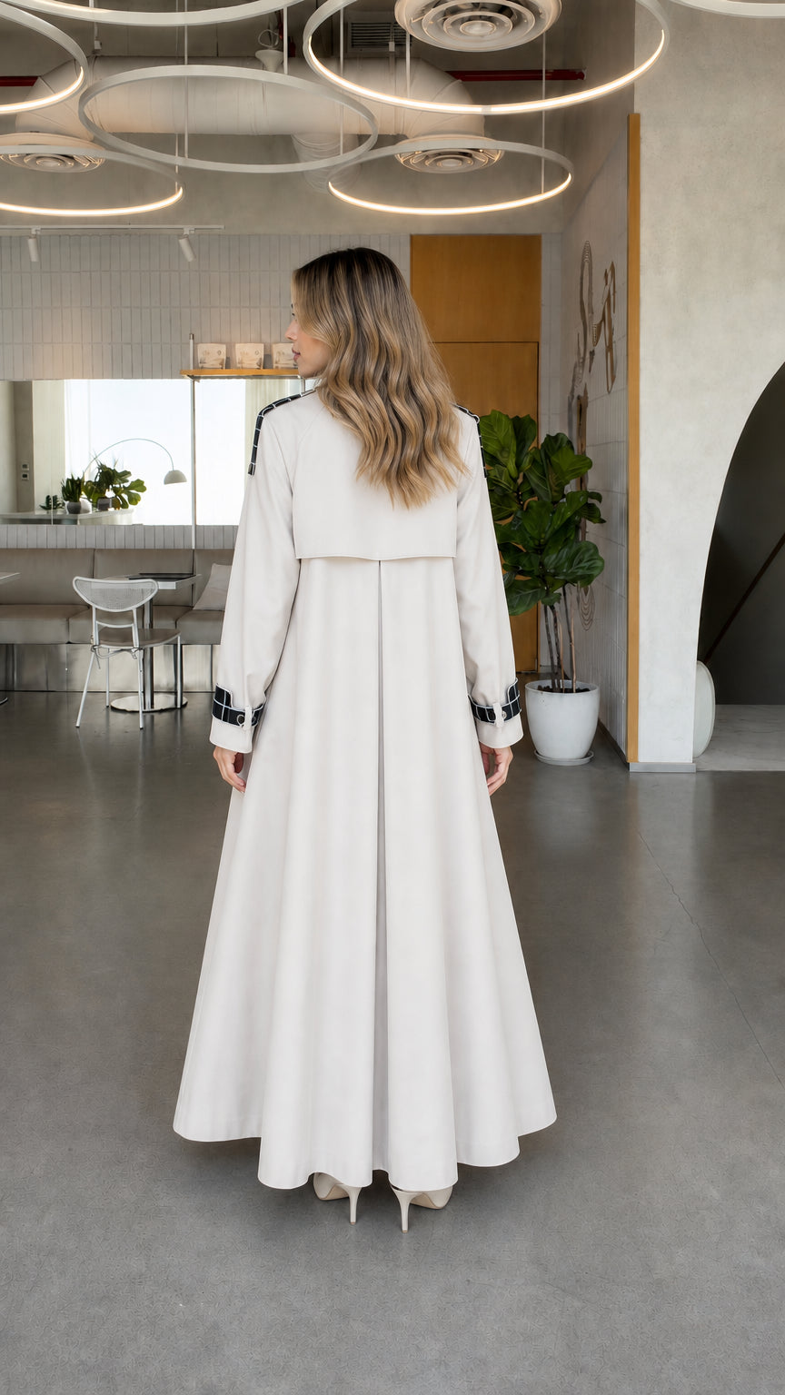 Back view of model wearing off white full-length trench coat showing storm flap detail