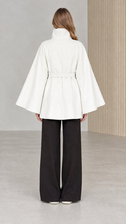 Back view of model wearing white high neck cape coat with belt