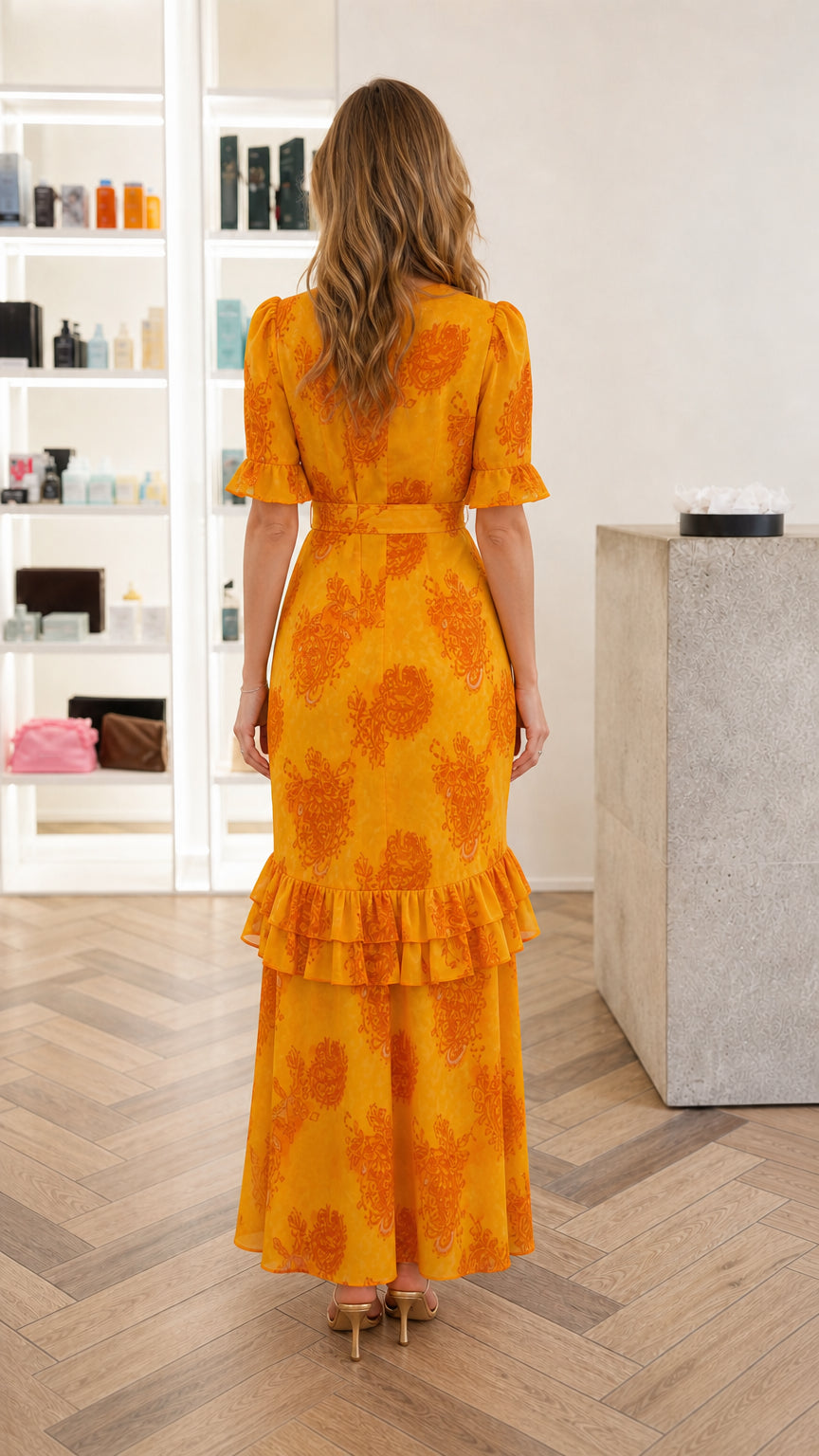 Back view of woman wearing Marigold yellow paisley belted maxi dress with tiered ruffled hem