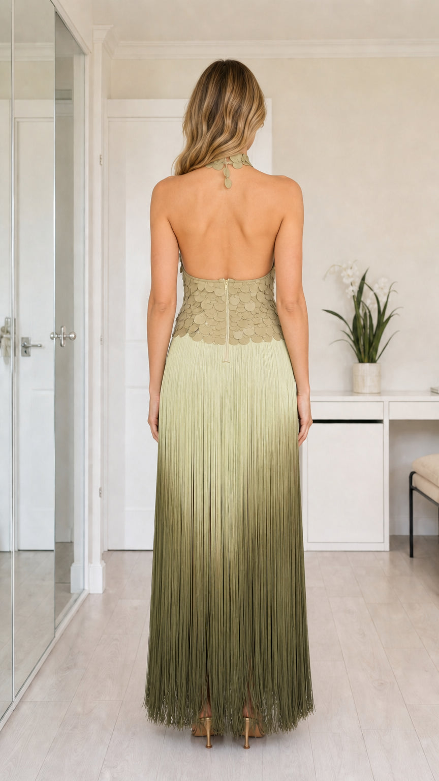Back view of sage green halter dress featuring open back and fringe skirt